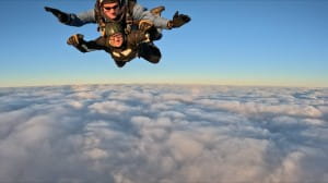Abby skydiving through the blue sky, clouds below