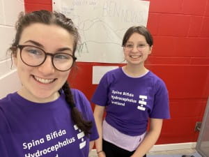 Eve and Murren stood in their school before their fundraising challenge. A tally chart of Ben Nevis laps in the background.