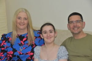 family of 3 people sit smiling at camera.