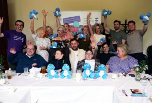 Group of individuals posing for a photo in front of a table featuring cuddly toys and cakes