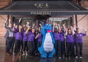 Staff team group around big blue dinosaur pointing at sky